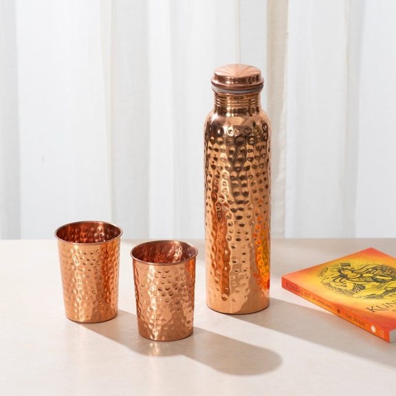 A hammered copper bottle with two matching cups from the Vedansh collection